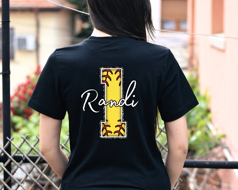 May include: Black t-shirt with a yellow and red softball letter I and the name "Randi" in white cursive writing.