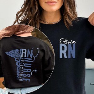 May include: Black sweatshirt with a blue and white graphic of a caduceus and the text "RN NURSE REGISTERED" on the back. The front of the sweatshirt has the text "Olivia RN" in blue and white.