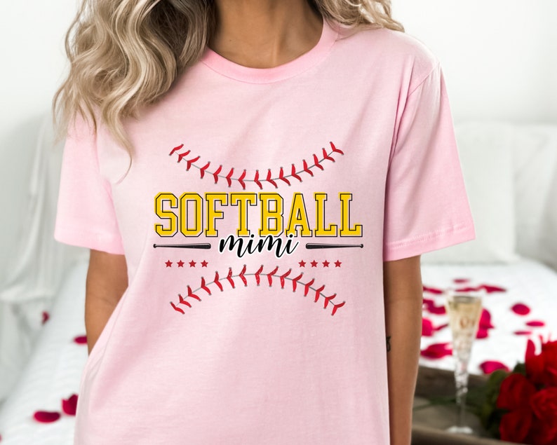 May include: Pink t-shirt with a softball graphic and the text "Softball mimi" in yellow letters.
