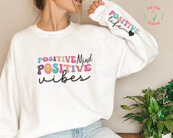 May include: White sweatshirt with the text "POSITIVE Mind POSITIVE vibes" in colorful letters with a heart design. The sleeve has the text "POSITIVE life" with a heart design.