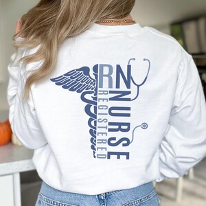 May include: White long-sleeve shirt with a blue graphic of a caduceus and the text "RN Registered Nurse".