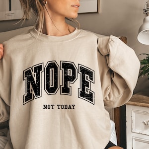 May include: A beige sweatshirt with a black graphic print that says "NOPE NOT TODAY" in a vintage collegiate style font.