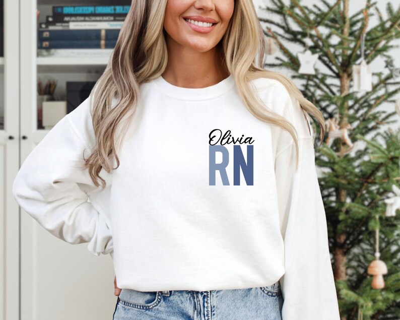 May include: White sweatshirt with the name Olivia and the letters RN in blue and gray on the front.