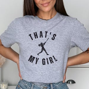 May include: Gray t-shirt with a black graphic of a girl playing baseball and the text "That's My Girl".
