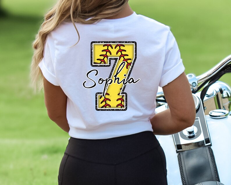 May include: White t-shirt with a yellow softball number 7 with red stitching and the name "Sophia" written in black cursive.