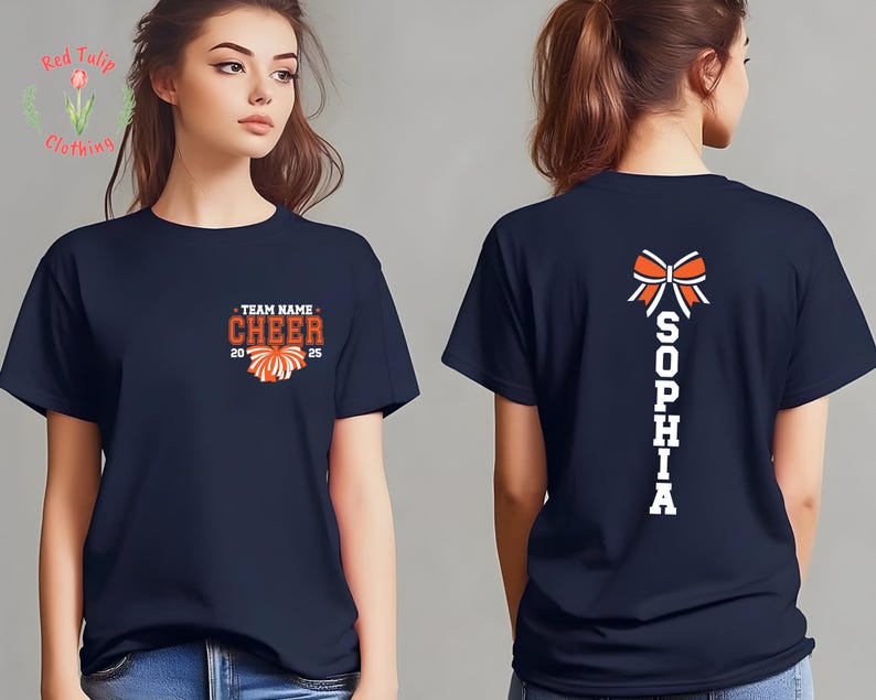 May include: A navy blue short-sleeve t-shirt featuring a front graphic with the text TEAM NAME CHEER 2025 and a pom-pom icon. The back of the shirt displays a large orange and white cheer bow graphic above the vertical white text SOPHIA.