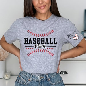 Peut inclure: T-shirt gris avec le texte "Baseball Mom" et un graphique de baseball. Le t-shirt a un c&oelig;ur rouge avec un graphique de baseball sur la manche et le nom "Olivia" &eacute;crit au-dessus.