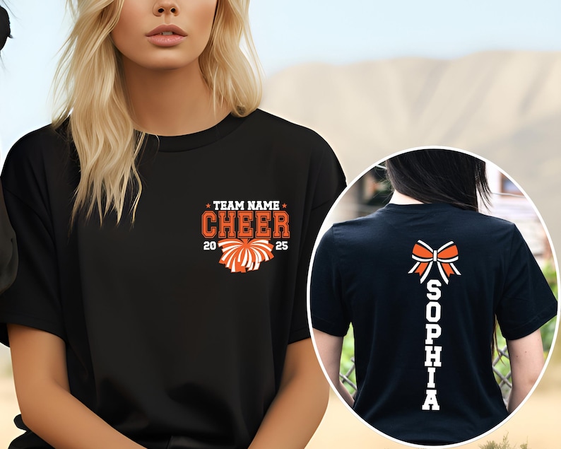 May include: A black t-shirt featuring a front graphic with the text TEAM NAME CHEER 2025 and an orange pom-pom. The back graphic displays a white and orange bow above the vertical text SOPHIA in white block letters on a black t-shirt background.