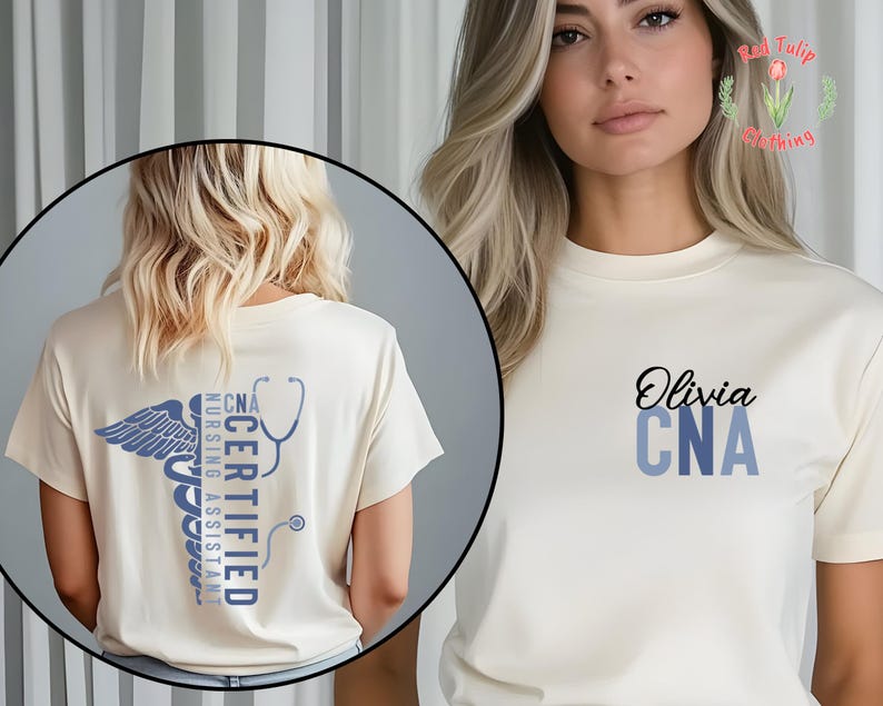 以下が含まれることがあります： クリーム色のTシャツ。黒い筆記体で「Olivia」と書かれ、その下に青い文字で「CNA」と書かれています。Tシャツの背面には、青いカドゥケウスのシンボルと「CNA CERTIFIED NURSING ASSISTANT」の文字、聴診器が描かれています。