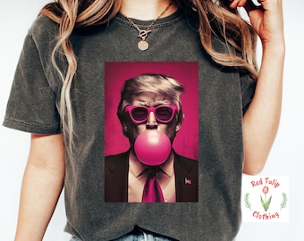 May include: A dark gray t-shirt with a pink and white graphic of a man wearing sunglasses and blowing a bubble. The graphic includes the text "Red Tulip Clothing".