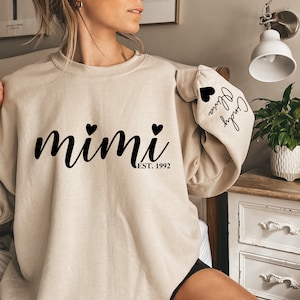 May include: A beige sweatshirt with the text "mimi est. 1992" and two small black hearts on the front. The left sleeve has the text "Crazy in love" with a black heart.