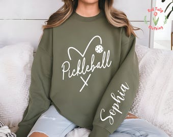 May include: A green sweatshirt with a white heart design that says "Pickleball" and a white paddle and ball. The sweatshirt has a white name "Sophia" on the sleeve.