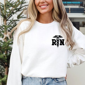 May include: White long-sleeved sweatshirt with a black graphic of a caduceus and the letters "RN".