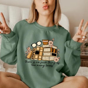 May include: Green sweatshirt with a stack of books, a cup of coffee, and glasses. The text on the sweatshirt reads "there is no such thing as too many books".
