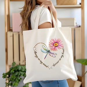 May include: White canvas tote bag with a colorful dragonfly and pink flower design. The text reads "Always on my mind...Forever in my heart."