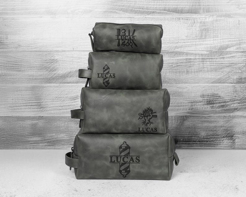 Puede incluir: Cuatro neceseres de cuero gris apilados. Cada bolsa tiene un dise&ntilde;o diferente con tem&aacute;tica de barber&iacute;a y el nombre "LUCAS" grabado. Las bolsas son de diferentes tama&ntilde;os y tienen cierre de cremallera.