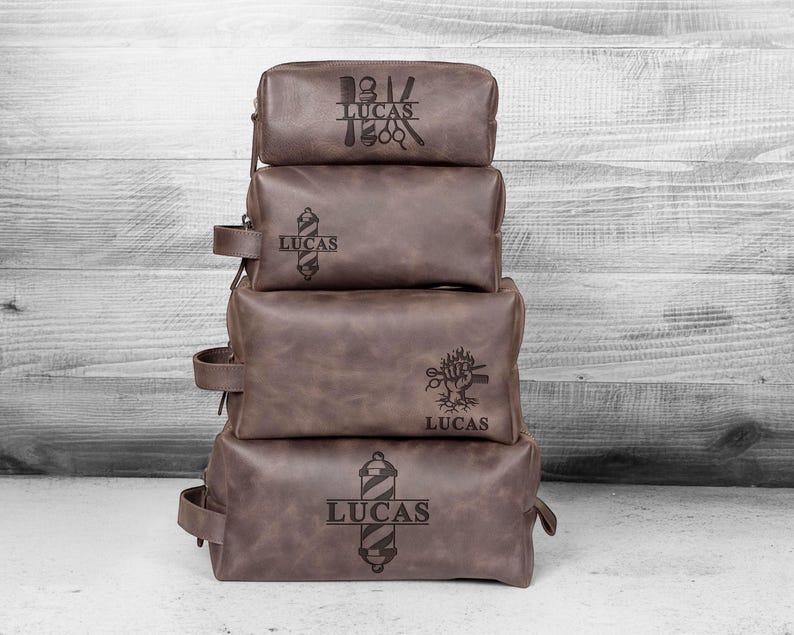Puede incluir: Cuatro neceseres de cuero marr&oacute;n apilados con texto personalizado y dise&ntilde;os tem&aacute;ticos de barber&iacute;a. Cada bolsa tiene un dise&ntilde;o diferente, incluyendo tijeras, un poste de barbero y el nombre "LUCAS". Las bolsas tienen un asa lateral.