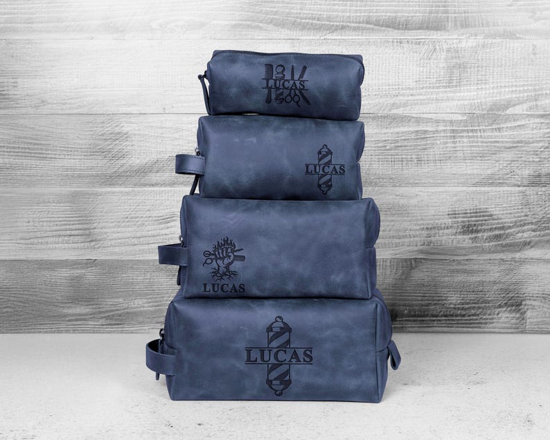 Puede incluir: Cuatro neceseres de cuero azul apilados, con dise&ntilde;os grabados en negro y el nombre "LUCAS". Cada bolsa tiene un dise&ntilde;o diferente, incluyendo un poste de barbero, un &aacute;rbol y un emblema vintage. Las bolsas son de diferentes tama&ntilde;os y tienen un asa lateral.