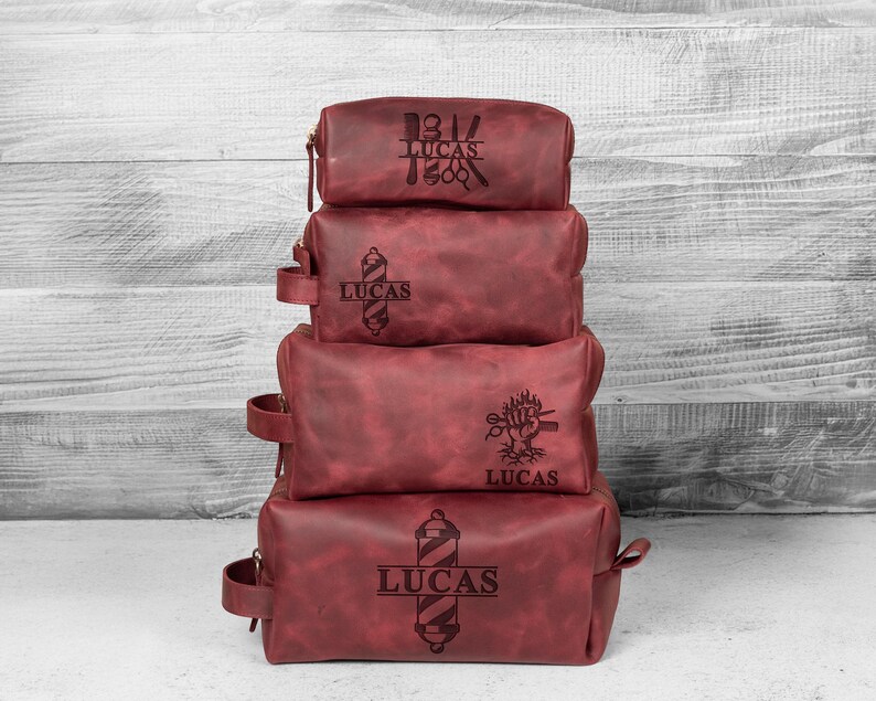 Puede incluir: Una pila de cuatro neceseres de cuero burdeos. Cada bolsa tiene cierre de cremallera y asa. Las bolsas est&aacute;n grabadas con dise&ntilde;os de barber&iacute;a y el nombre "LUCAS".