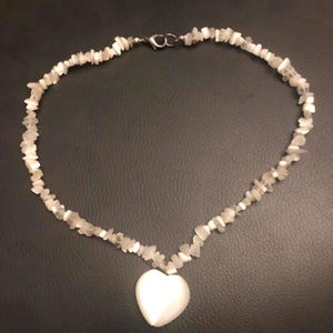 May include: A white stone necklace with a heart pendant. The necklace features small, irregular-shaped white stones strung together, forming a chain. A larger, heart-shaped white stone hangs as a pendant, creating a simple yet elegant design.