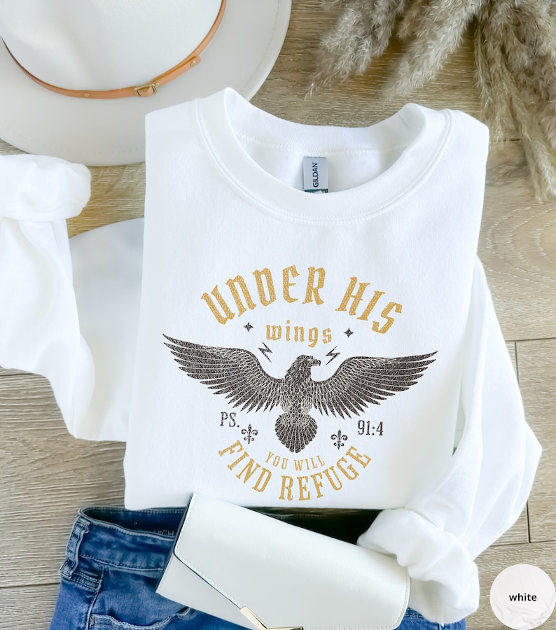 May include: White sweatshirt with a gold graphic of an eagle with the text "Under His Wings You Will Find Refuge" and the scripture reference "Ps. 91:4".
