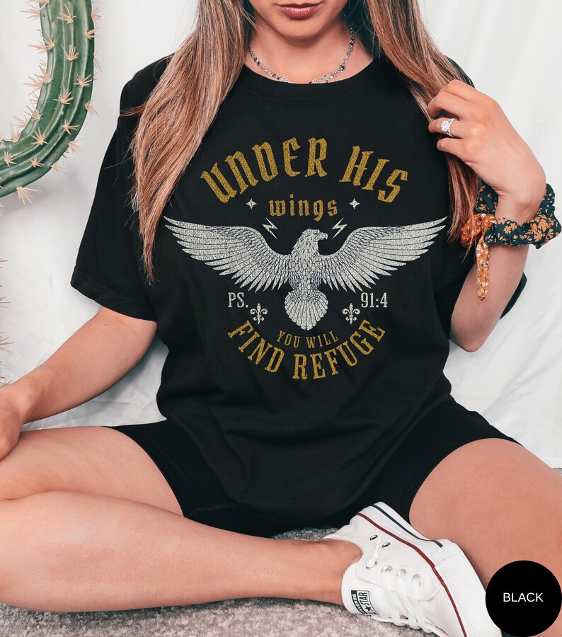 May include: Black t-shirt with a gold graphic of an eagle with the text "Under His Wings" and "Ps. 91:4 You Will Find Refuge".