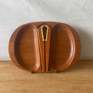 May include: A wooden serving tray with two compartments and a built-in nutcracker. The tray is made of dark wood and has a natural finish. The nutcracker is made of metal with a gold finish.