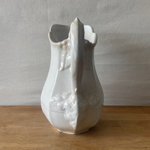 May include: White ceramic pitcher with a floral design and a handle. The pitcher has a rounded body and a wide mouth.