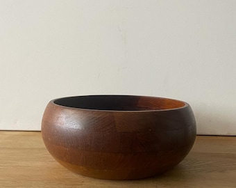 May include: A large, round wooden bowl made of dark brown wood. The bowl is made of individual pieces of wood that are fitted together.