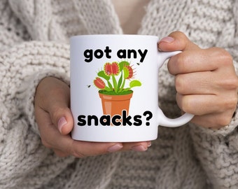 Uma caneca dupla face engraçada com estampa de Vênus e a inscrição "Got Any Snacks?" (Tem algum lanche?) – perfeita para amantes de plantas com senso de humor!