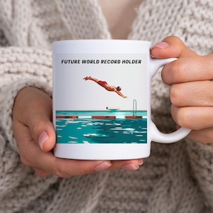 May include: White ceramic mug with a blue, green, and white illustration of a person diving into a pool. The text "FUTURE WORLD RECORD HOLDER" is printed in black on the mug.