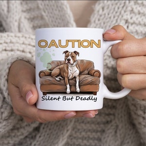 Op de afbeelding: Witte keramische mok met een bruine en witte pit bull die op een bruine bank zit. De mok heeft de tekst "CAUTION Silent But Deadly" in gouden letters.