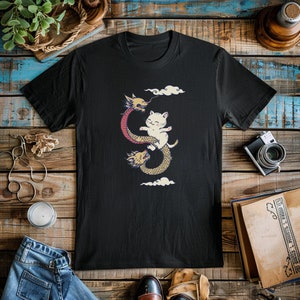 K&ouml;nnte beinhalten: Schwarzes T-Shirt mit einem Aufdruck eines wei&szlig;en Katers, der auf einem roten und gelben Drachen reitet.