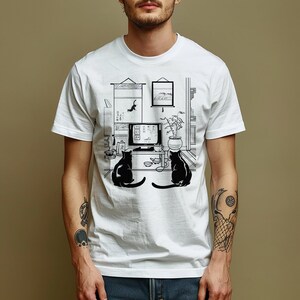 May include: White t-shirt with a black and white illustration of two cats watching television in a room with a potted plant and a scroll hanging on the wall.