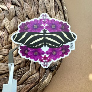 May include: A black and white zebra butterfly sticker with a purple flower border. The sticker has the text "Luna Lupe" and "31.08.2021" on it.