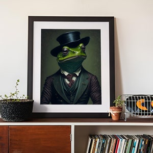 May include: A framed print of a green frog wearing a black top hat and a suit. The frog is looking directly at the viewer. The background is a dark green.