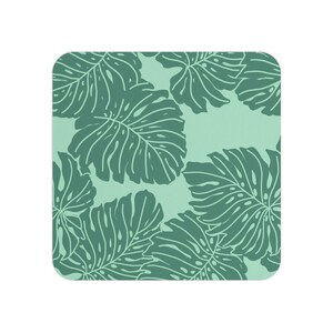 Op de afbeelding: Een vierkante onderzetter met een herhalend patroon van donkergroene monstera-bladeren op een licht mintgroene achtergrond. De onderzetter heeft afgeronde hoeken en een plat oppervlak met een botanische print met gedetailleerde bladnerven.