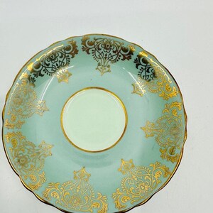 May include: A light blue saucer with a gold floral pattern. The saucer has a scalloped edge and a white center.