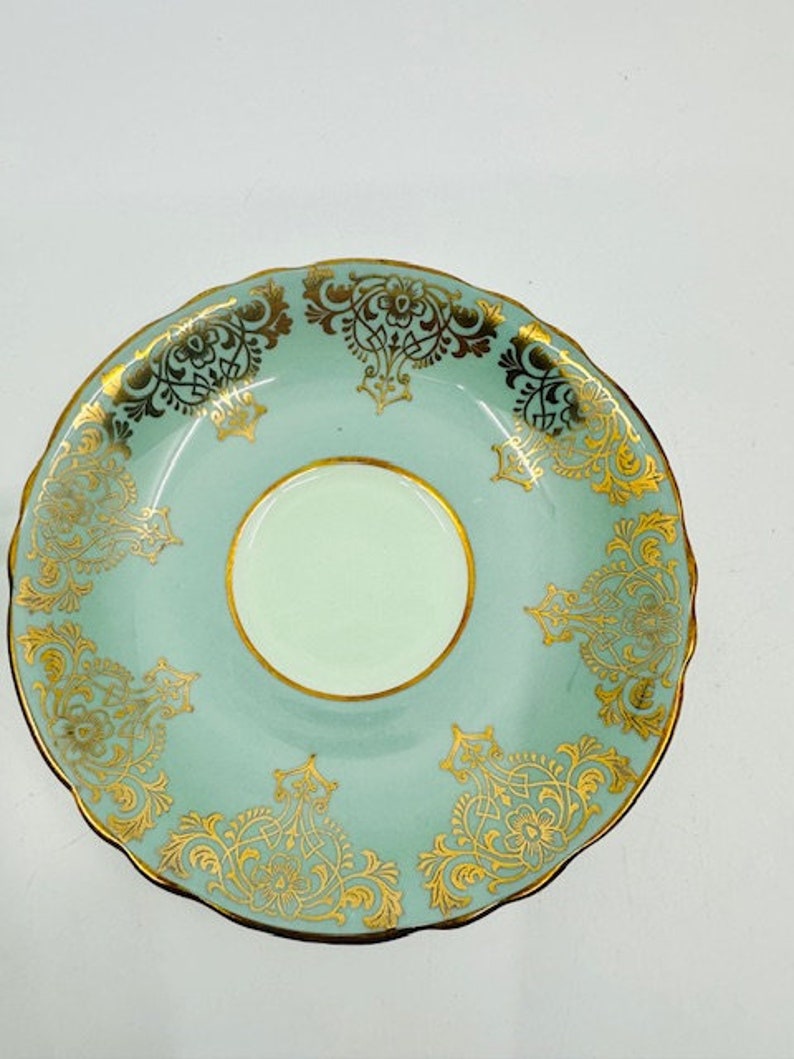 May include: A light blue saucer with a gold floral pattern. The saucer has a scalloped edge and a white center.