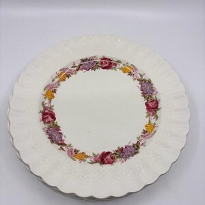 May include: A set of white ceramic dinner plates with a scalloped edge and a floral design in shades of pink, yellow, and purple.