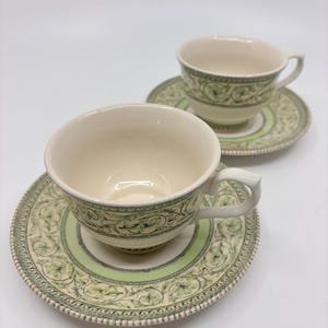 Puede incluir: Una taza de cerámica blanca con un asa negra y el texto "But First, Coffee" en un estilo manuscrito. La taza está sobre una superficie blanca. La taza mide aproximadamente 10 cm de alto.