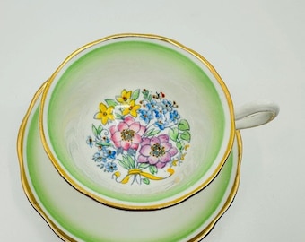 May include: A green and white teacup and saucer set with a floral design. The cup and saucer have a gold trim.