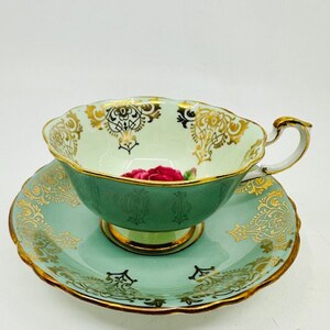 May include: A green teacup and saucer set with gold trim and a pink rose design. The set is made of fine china and has a delicate, elegant look.