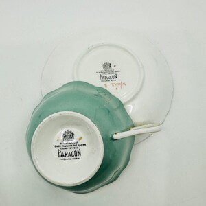 May include: A green teacup and saucer set with a white floral design. The teacup and saucer are made by Paragon, England. The saucer has a gold rim.