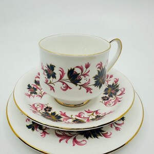 May include: A white teacup and saucer set with a floral pattern in shades of pink, black, and gold. The set features a delicate floral design with intricate details.