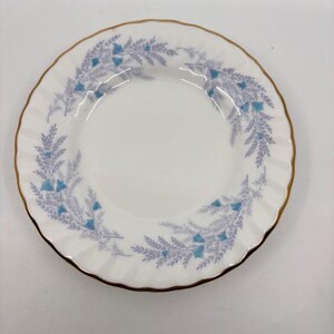 May include: White porcelain plate with a gold rim and a scalloped edge. The plate features a delicate blue and lavender floral pattern around the rim. A classic piece for serving appetizers or desserts.