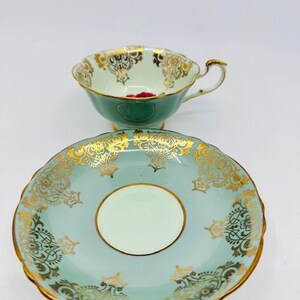 May include: A vintage teacup and saucer set with a delicate floral design in gold and pink on a light green background.