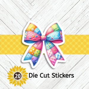 May include: A die-cut sticker featuring a colorful patchwork bow with pink, blue, yellow, and green squares. The sticker has a white border and is set against a yellow banner and a white wood-grain background. The text "20 Die Cut Stickers" is also present.