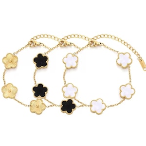 May include: Two gold-colored chain bracelets with flower-shaped charms. One bracelet features gold-colored and black charms, while the other has gold-colored and white charms. The bracelets have a lobster clasp closure.