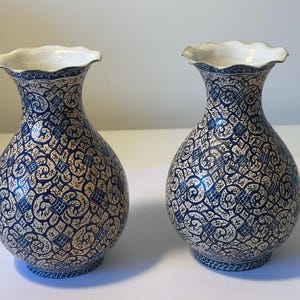May include: A pair of matching ceramic vases with a bulbous body and a flared, scalloped rim. The exterior features a dense, intricate pattern of dark blue swirling lines and geometric shapes set against a cream-colored background.